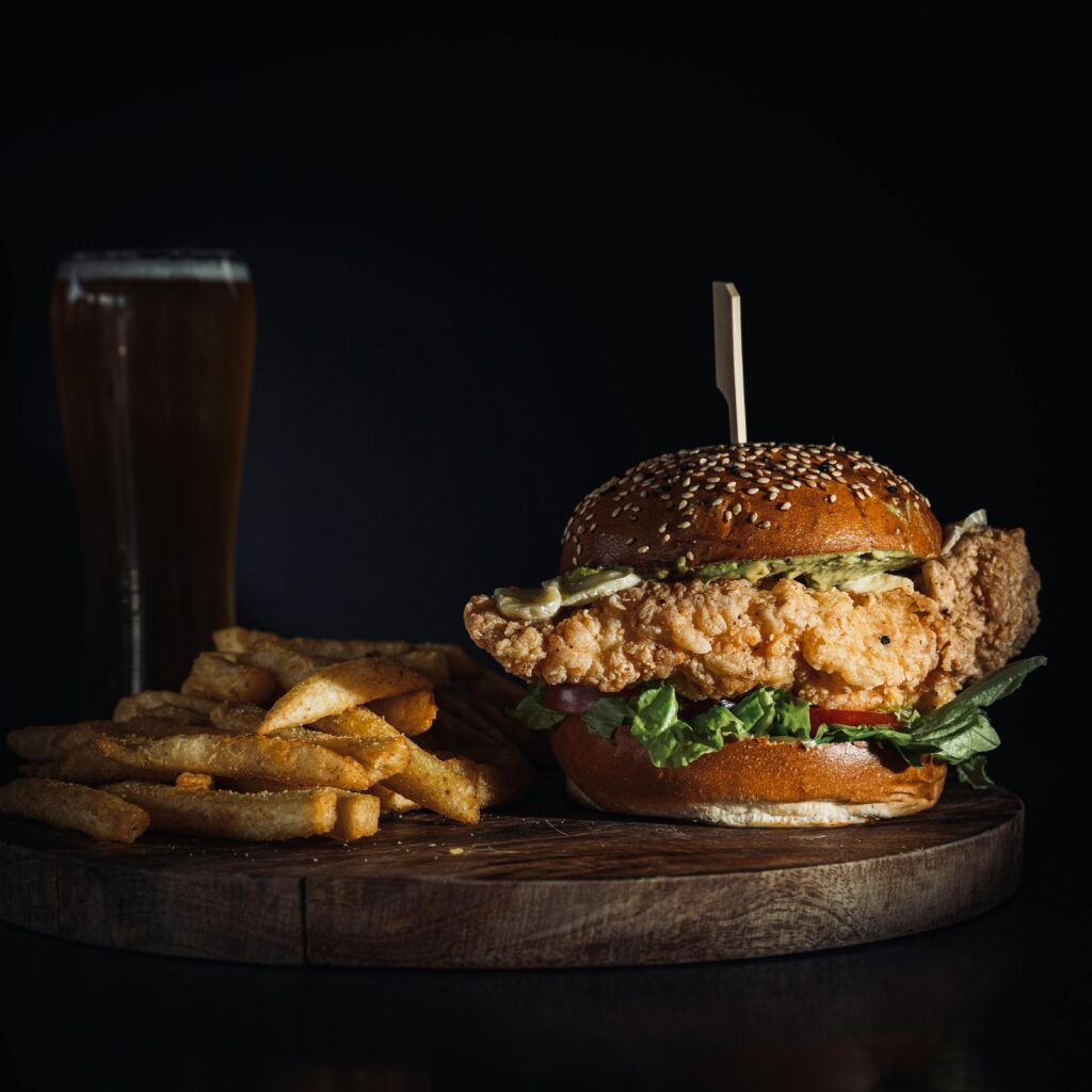 Delicious crispy chicken sandwich served with fries and a pint of beer on a wooden board.